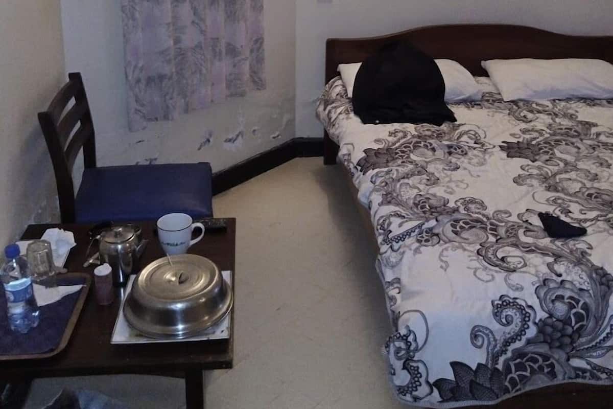 Ett litet hotellrum med en säng, ett bord med en vattenkokare, en kopp och en stol.