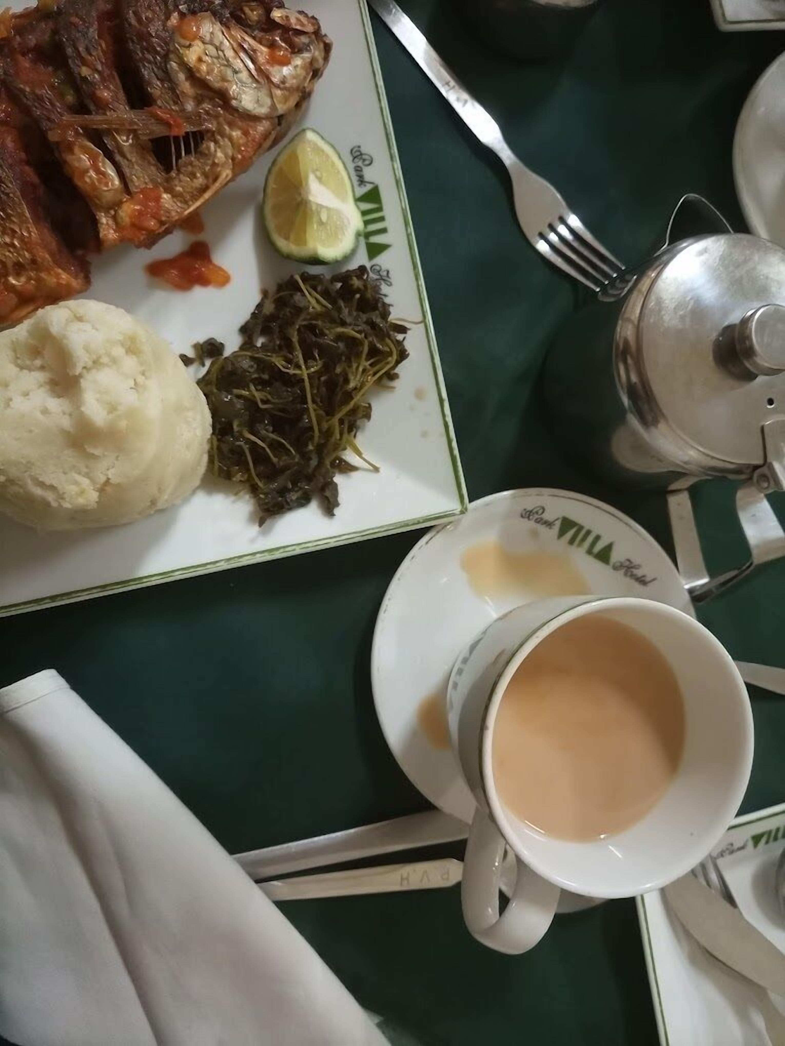 Un plato con pescado, puré de papas, vegetales verdes y una taza de té sobre una mesa.