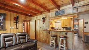 A cozy cabin interior with a leather sofa, wooden bar stools, and a kitchen area. - All in Cabin (Big Bear Lake)