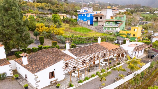 Un bâtiment traditionnel de couleur blanche, avec un toit en tuiles, un mur en pierre et un petit jardin agrémenté de plantes en pot.