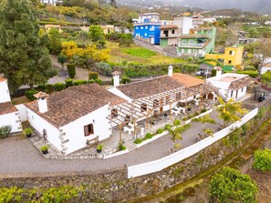 Un bâtiment traditionnel de couleur blanche, avec un toit en tuiles, un mur en pierre et un petit jardin agrémenté de plantes en pot.