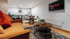 A modern living room with a sofa, a coffee table, and a TV mounted on the wall displaying 'NETFLIX'. - Spacious City Apartment| 2 bd/2 bth| Free Parking (Merseyside)