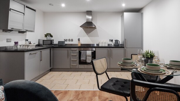 A modern kitchen with grey cabinets, stainless steel appliances, and a dining area with a glass table set for four. - Spacious City Apartment| 2 bd/2 bth| Free Parking (Merseyside)