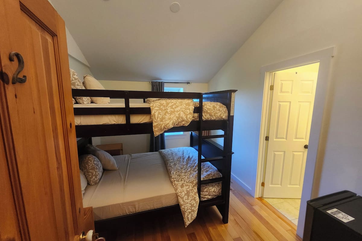Habitación con literas, una puerta de madera, una puerta blanca y un cesto de basura.