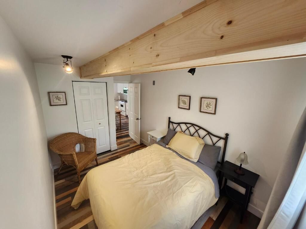A bedroom with a bed, a chair, a nightstand, and a door leading to a staircase.