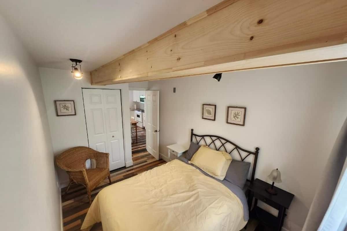 Un dormitorio con cama, una silla, una mesita de noche y una puerta que da a una escalera.