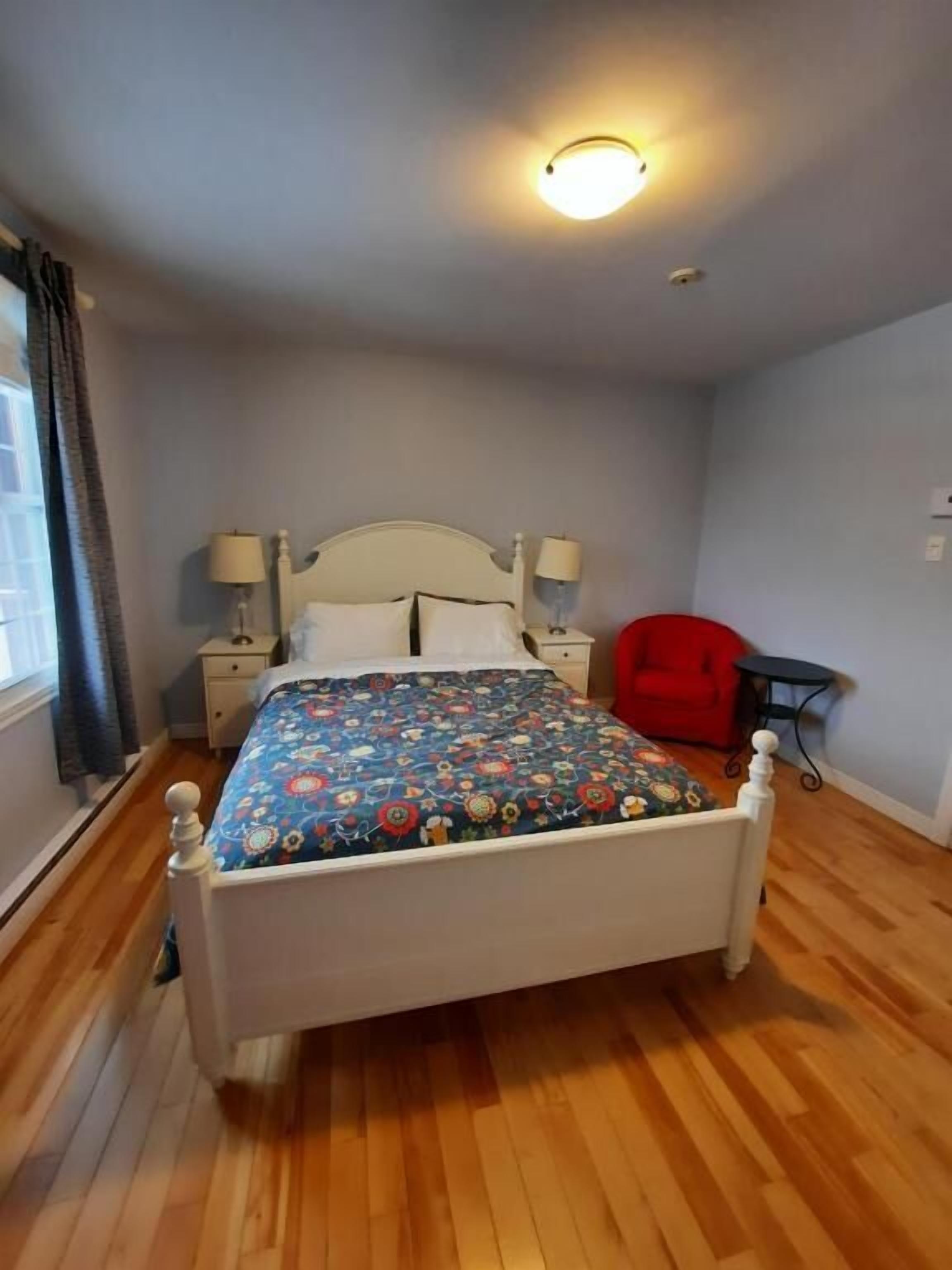 A bedroom with a bed, bedside tables, a red chair, and a small table.