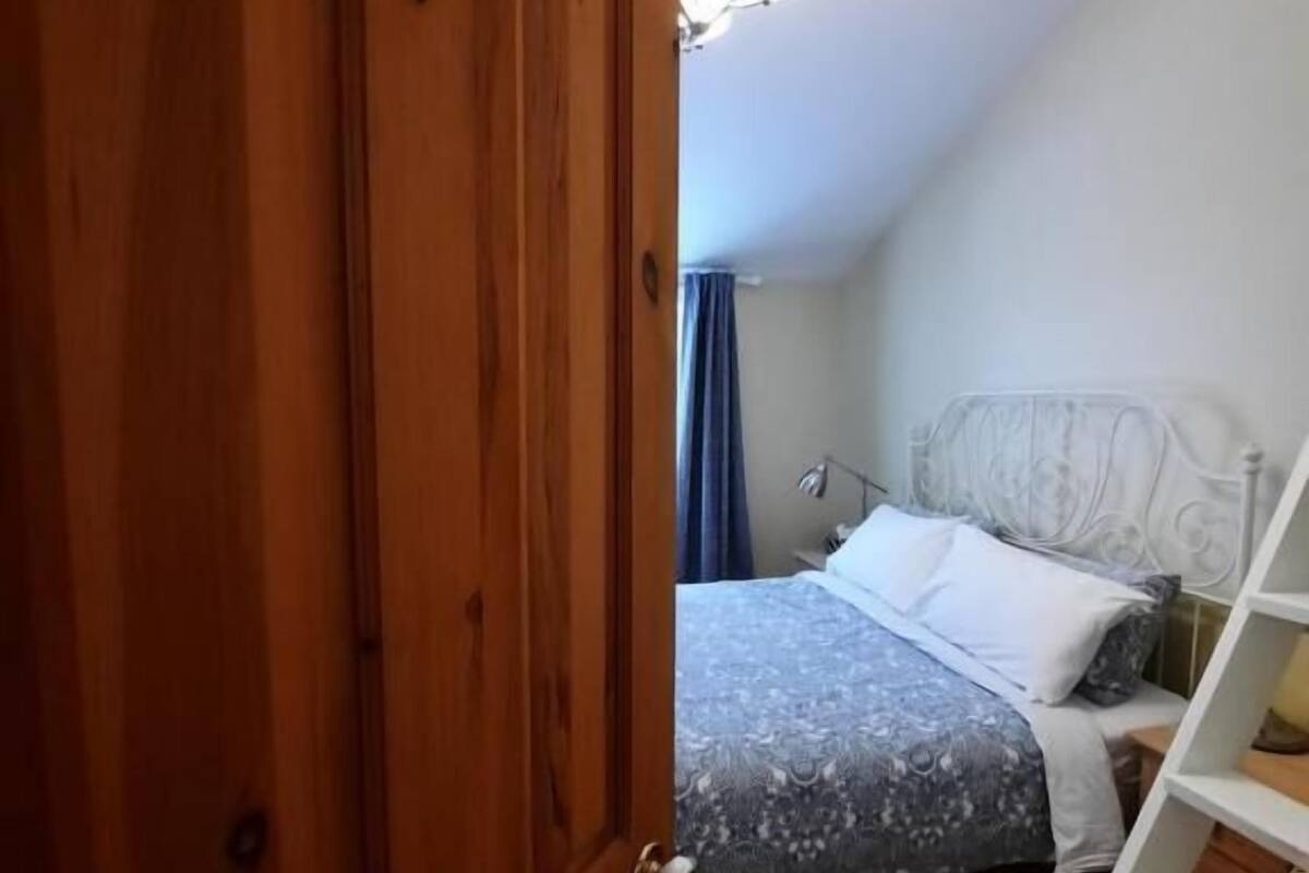 Un dormitorio con una puerta de madera, una cama con ropa de cama estampada, un cabecero blanco y una estantería blanca.