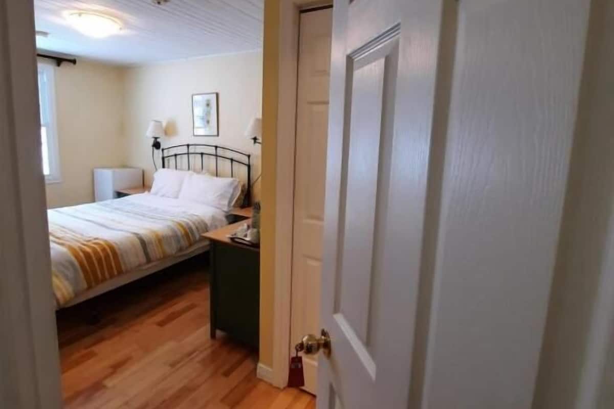 Un dormitorio con cama, mesita de noche y puerta que da a otra habitación.