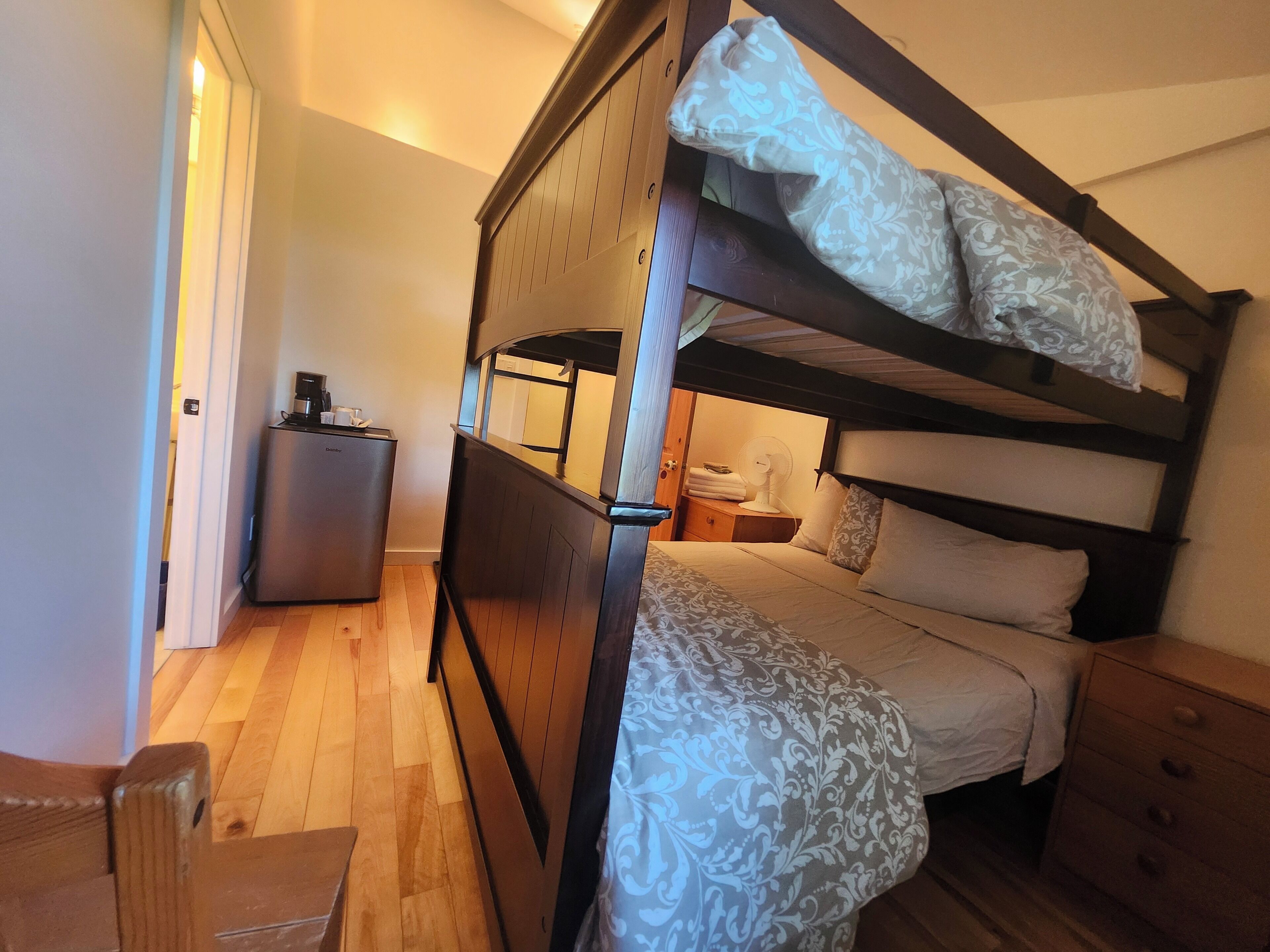 A bunk bed with a bedside table, a small refrigerator, and a nightstand with a lamp.