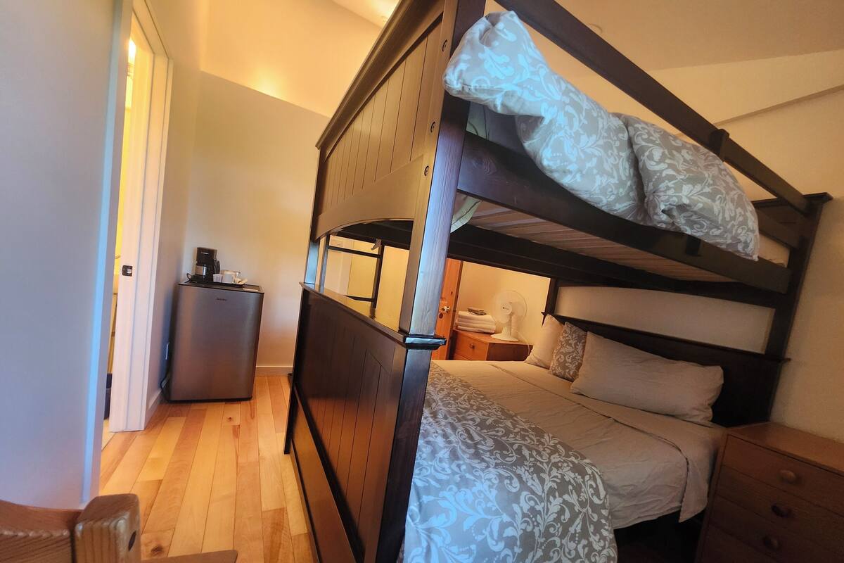 A bunk bed with a bedside table, a small refrigerator, and a nightstand with a lamp.