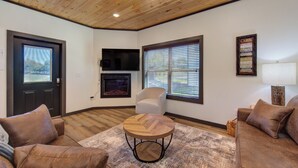 A living room with a fireplace, a TV mounted on the wall, and a wooden ceiling. - *Charming 4BD Lodge Near TOWN! Fire Pit + Hot Tub* (Sevierville)