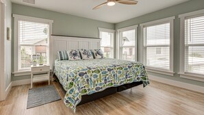 A bedroom with a bed, a ceiling fan, and large windows.