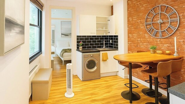 A modern kitchen with a black and white backsplash, a wooden dining table with two chairs, and a large wall clock. - Central London 2BR Near Piccadilly Circus for 4 (London)