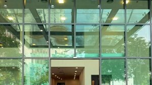 Une entrée moderne avec un tapis rouge menant à l’intérieur, de grandes fenêtres en verre et un paillasson à l’entrée.
