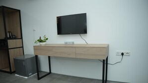 Un bureau moderne, avec un bureau en bois, un téléviseur à écran plat fixé au mur, un petit réfrigérateur gris et une plante en pot.