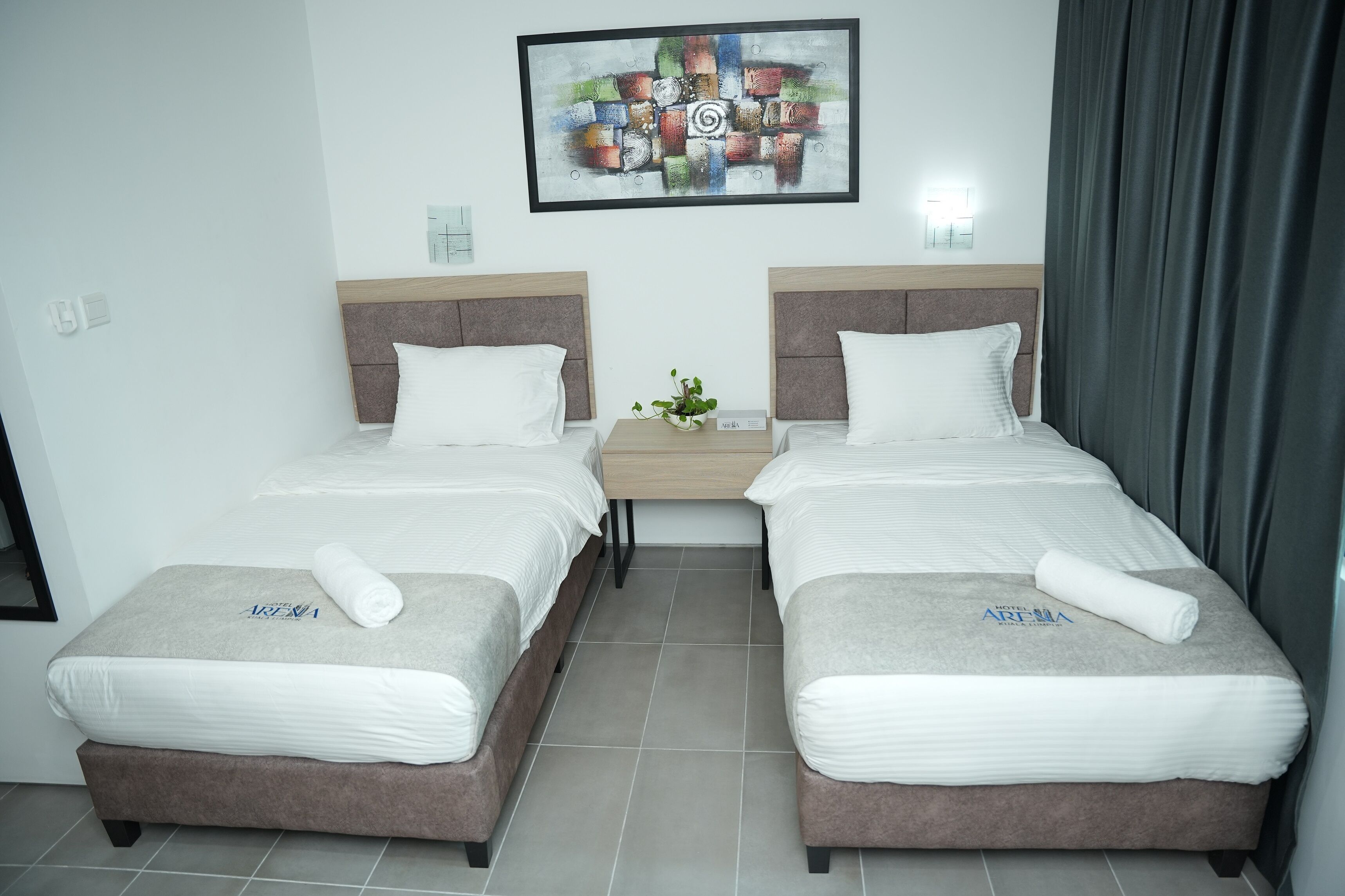 A hotel room with two beds, each with a headboard, a small bedside table with a plant, and a wall-mounted artwork.