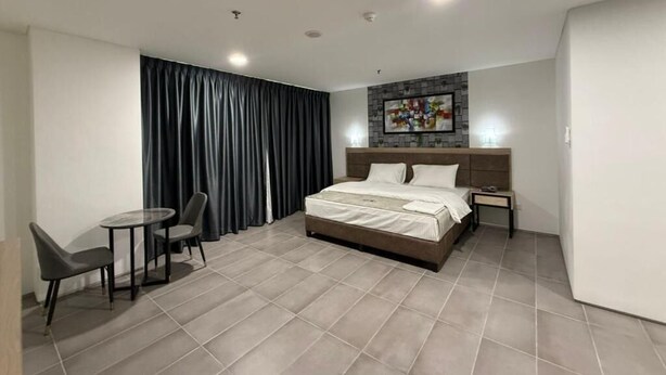 Une chambre d’hôtel moderne avec un grand lit, une petite table avec des chaises, une table de chevet et un tableau au mur.