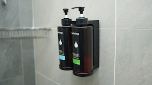 Deux distributeurs de savon noir, équipés de pompes, sont fixés à un mur recouvert de carreaux.