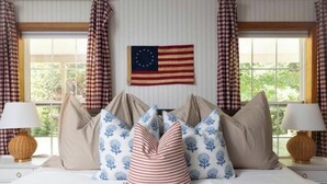 A hotel room with a bed, pillows, a flag on the wall, and curtains. - Acadia Escape: Hot Tub, Sauna, Game Room, Fire Pit (Mount Desert)