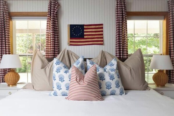 A hotel room with a bed, pillows, a flag on the wall, and curtains. - Acadia Escape: Hot Tub, Sauna, Game Room, Fire Pit (Mount Desert)