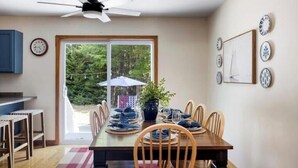 A dining area with a table set for four, a ceiling fan, and a view of the outdoors through a sliding door. - Acadia Escape: Hot Tub, Sauna, Game Room, Fire Pit (Mount Desert)