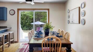 A dining area with a table set for four, a ceiling fan, and a view of the outdoors through a sliding door.
