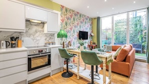 A modern kitchen with white cabinets, a marble backsplash, and a dining area with green chairs and a wooden table.