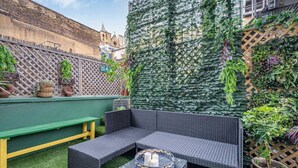 A rooftop patio with a dark wicker sofa, a green bench, and a small table with candles.