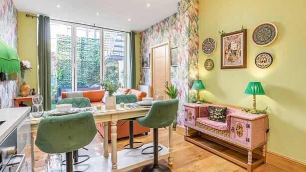 A dining area with a wooden table, green chairs, and a pink cabinet with a green lamp.