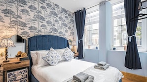 A neatly made bed with pillows, a bedside table with a lamp, and a window with curtains.