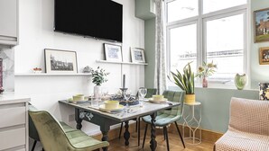 A dining area with a table set for four, surrounded by chairs, a television mounted on the wall, and framed pictures on the shelves.