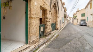 A narrow street with stone buildings, a green gate, and a parked car. - Unique Apartment with Parking and Wi-Fi (Saint-Thibéry)