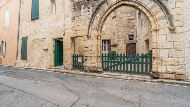 A stone building with a green door and a white sign above it. - Unique Apartment with Parking and Wi-Fi (Saint-Thibéry)