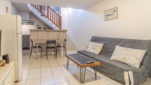 A living room with a grey sofa, a coffee table, and a dining area with chairs and a small table. - Unique Apartment with Parking and Wi-Fi (Saint-Thibéry)