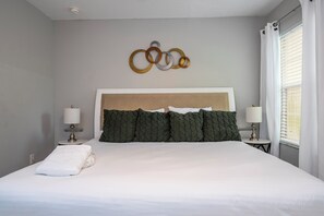 A neatly made bed with white linens, a headboard with a textured design, and a wall-mounted decorative piece.