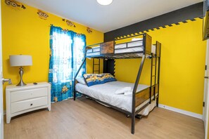 A bunk bed room with a white nightstand, a lamp, and a window with blue curtains.