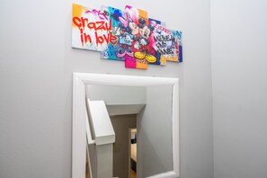 Une pièce avec une porte blanche, un mur blanc et une œuvre d’art colorée accrochée au-dessus de la porte.