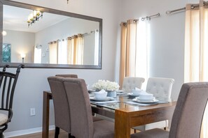 Un coin repas avec une table en bois, quatre chaises, un grand miroir et un lustre.