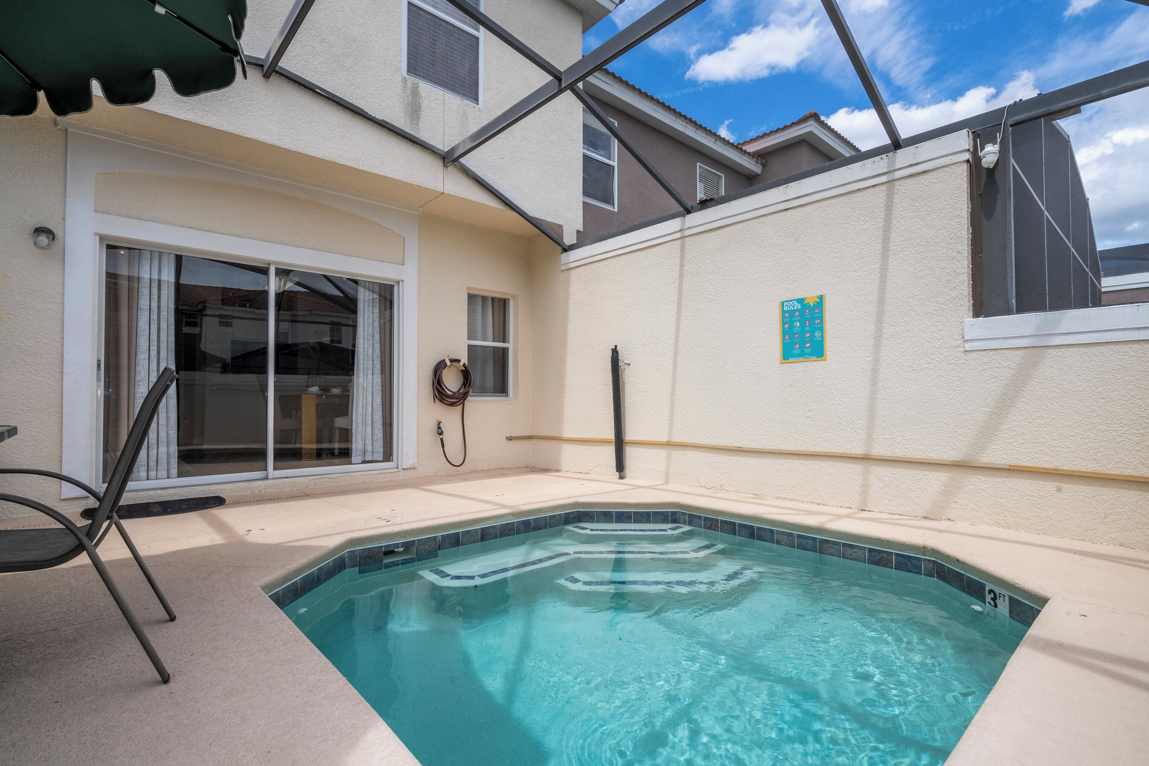 A swimming pool with a tiled edge, a covered patio area, and a sliding glass door.