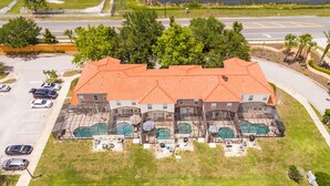 A multi-story building with a red roof, a swimming pool, and a parking lot. - 4BR Bella Vida Villa with Pool, BBQ & Themed Rooms near Disney (Kissimmee)