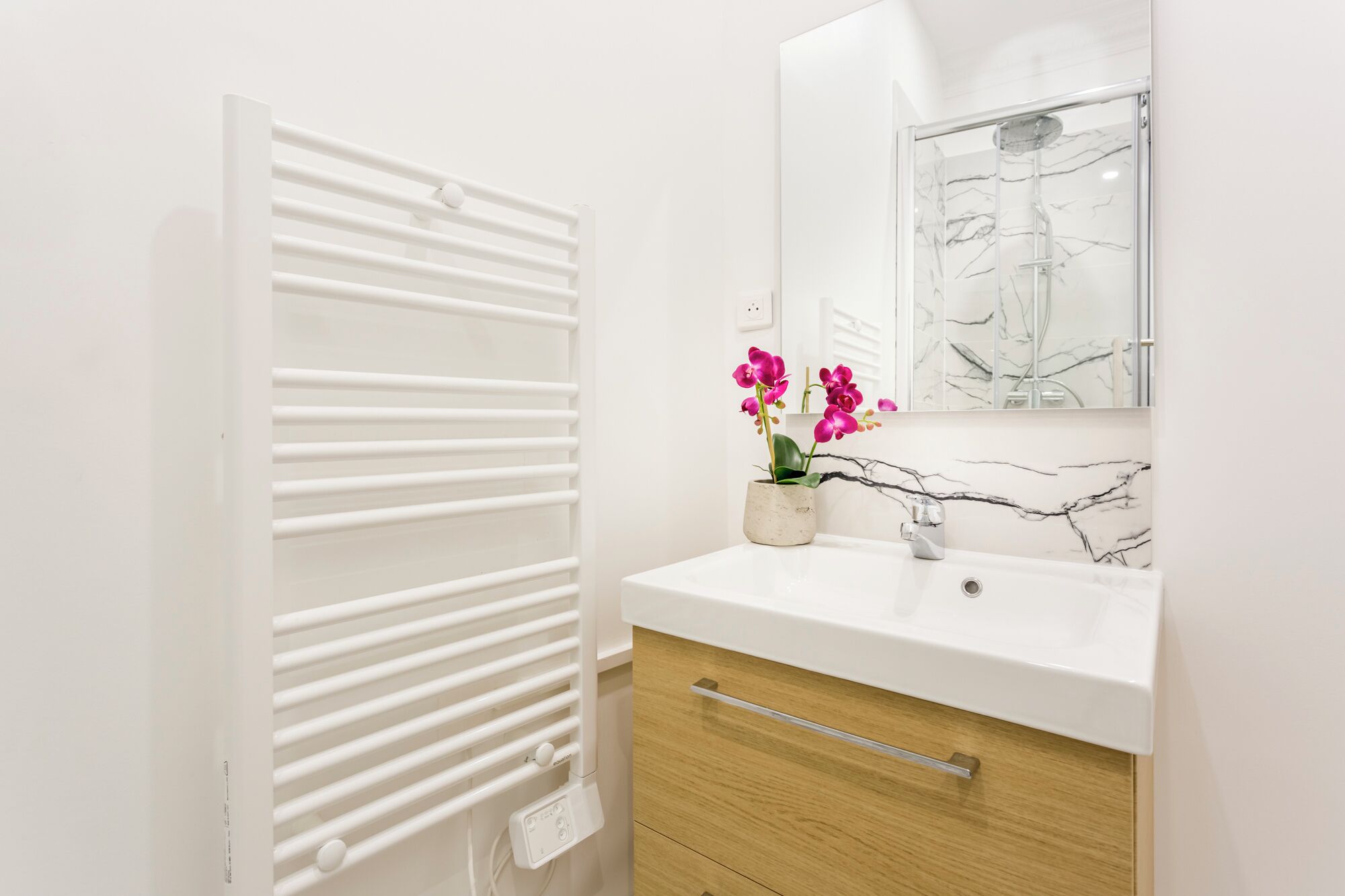 Un baño con un radiador blanco, un lavabo con salpicadero de mármol y un espejo sobre el lavabo.