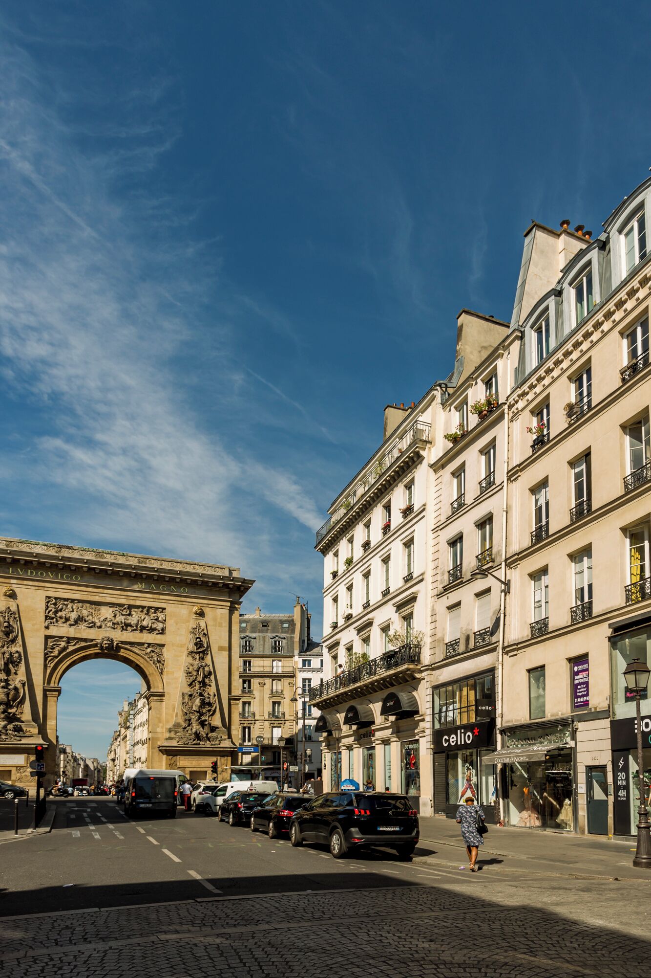 A street scene with an archway, buildings, shops, and a cobblestone street.