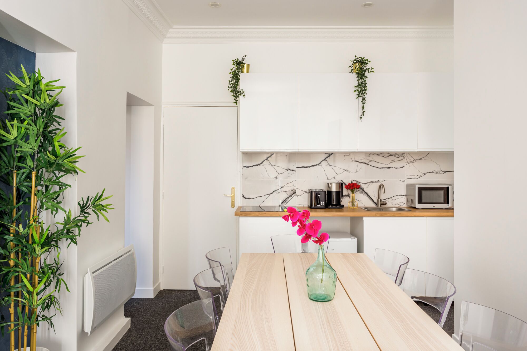 Een moderne keuken met witte kastjes, een marmeren spatwand en een houten aanrecht. Er staat een koffiezetapparaat, een magnetron en een vaas met bloemen op het aanrecht.