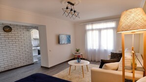 A modern living room with a sofa, a coffee table, and a TV. There is a brick wall and a window with curtains. - KAYARAN home (Gyumri)