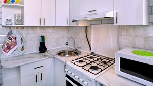 A compact kitchen with white cabinets, a stainless steel sink, a gas stove, and a microwave. - KAYARAN home (Gyumri)