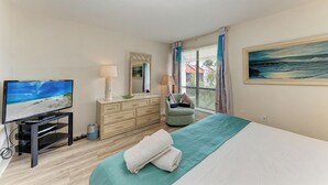 A bedroom with a bed, a TV on a stand, a dresser, a chair, and a painting on the wall. - Runaway Bay 209 - Waterview Condo with Heated Pool and Tennis (Bradenton Beach)