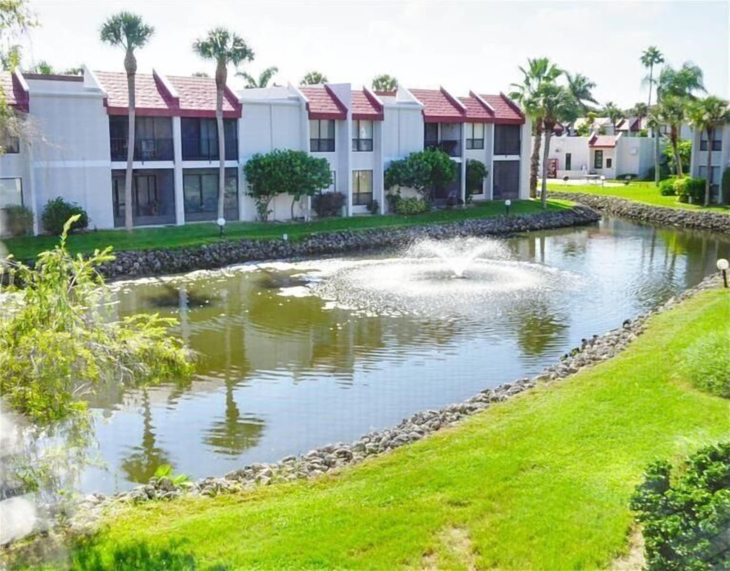 A hotel with a swimming pool, surrounded by well-maintained lawns and palm trees.