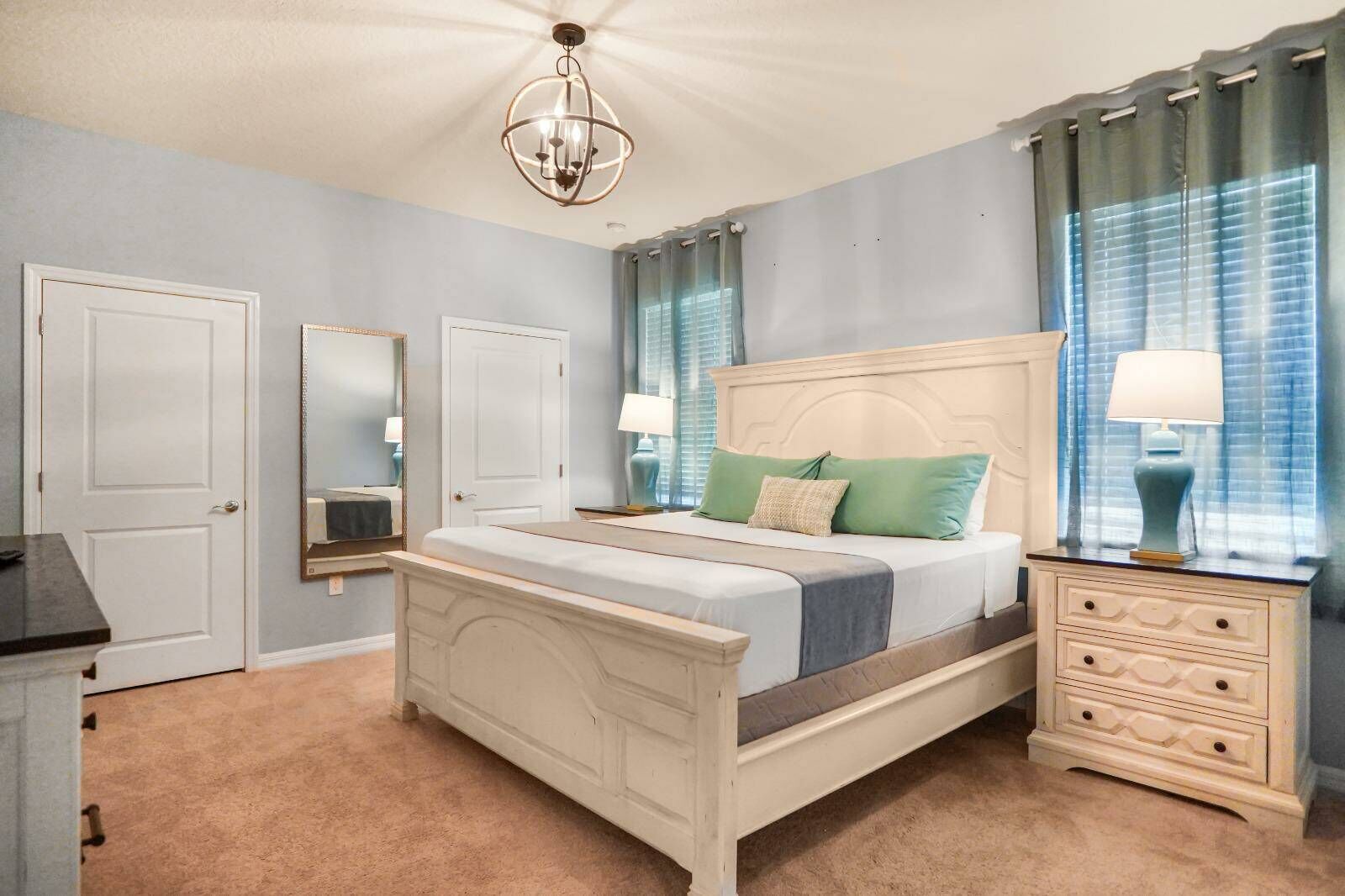 Une chambre à coucher avec un lit blanc, deux tables de chevet avec des lampes, une commode et un lustre.