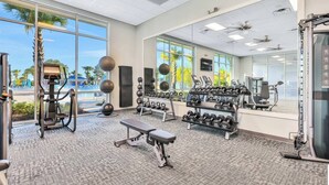 A modern gym with various exercise equipment, large windows, and a view of palm trees. - Orlando Escape • 8BR • Jacuzzi, Cinema & Arcade (Davenport)